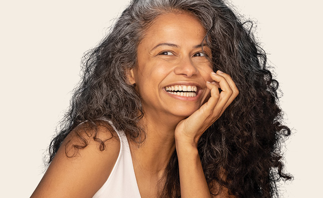 Femme aux longs cheveux bouclés se tenant le menton avec une main en souriant.