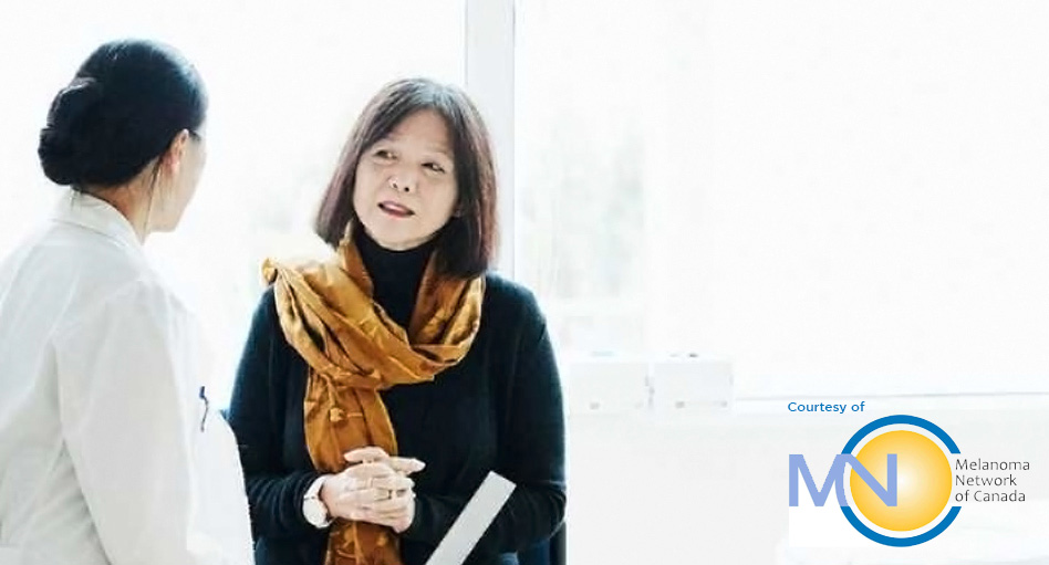 Woman with a scarf around her neck standing and listening to her dermatologist