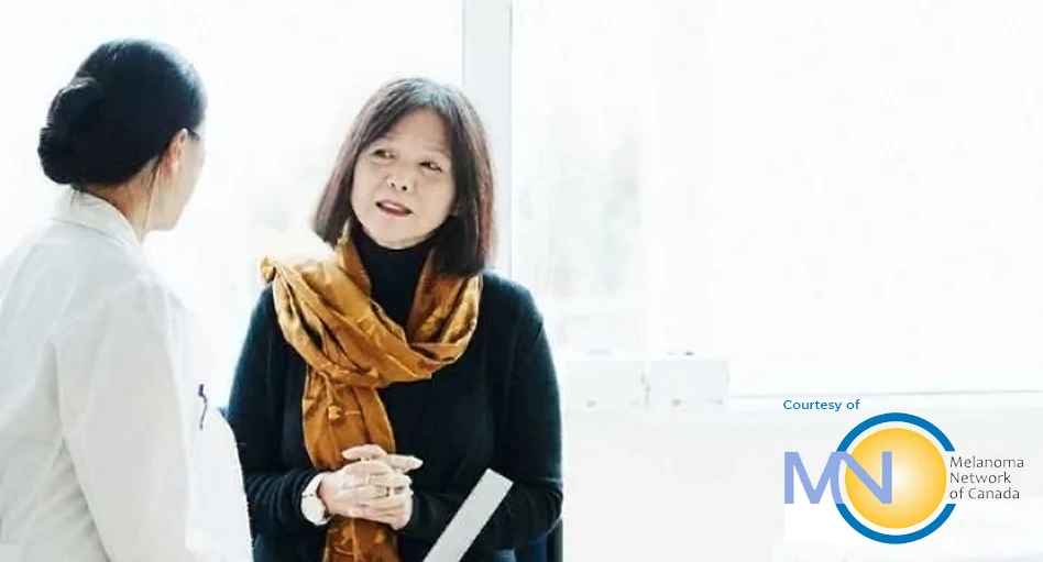 Woman with a scarf around her neck standing and listening to her dermatologist