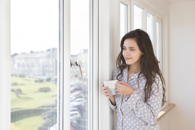 Femme debout près d'une fenêtre avec un café