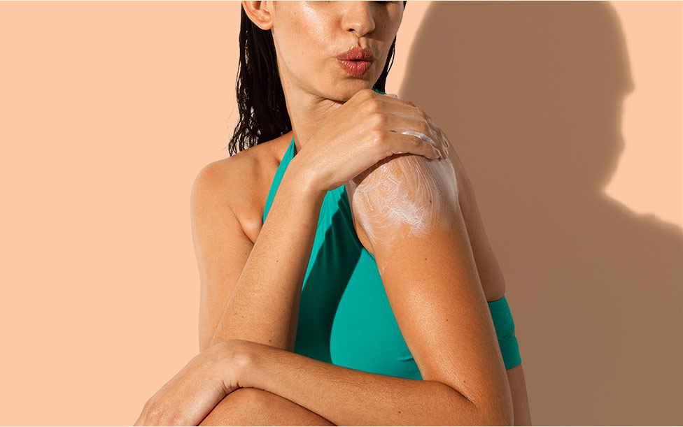 Woman applying Aveeno® sunscreen lotion on her shoulder