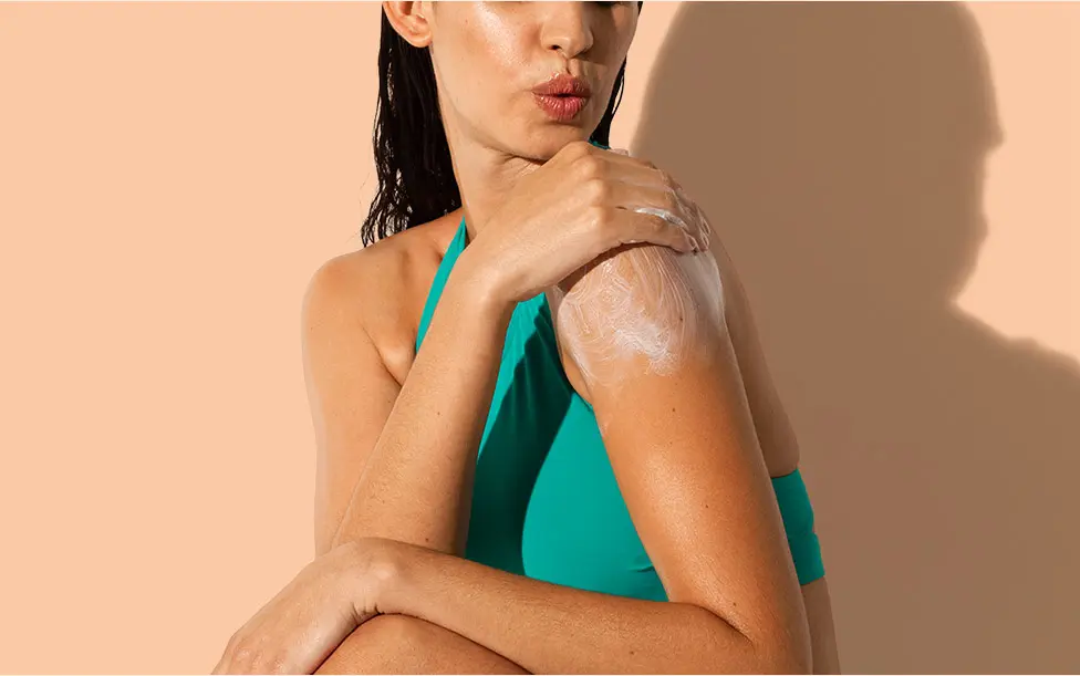 Woman applying Aveeno® sunscreen lotion on her shoulder
