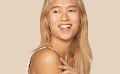 Une femme aux longs cheveux blonds regarde par-dessus son épaule gauche en souriant.