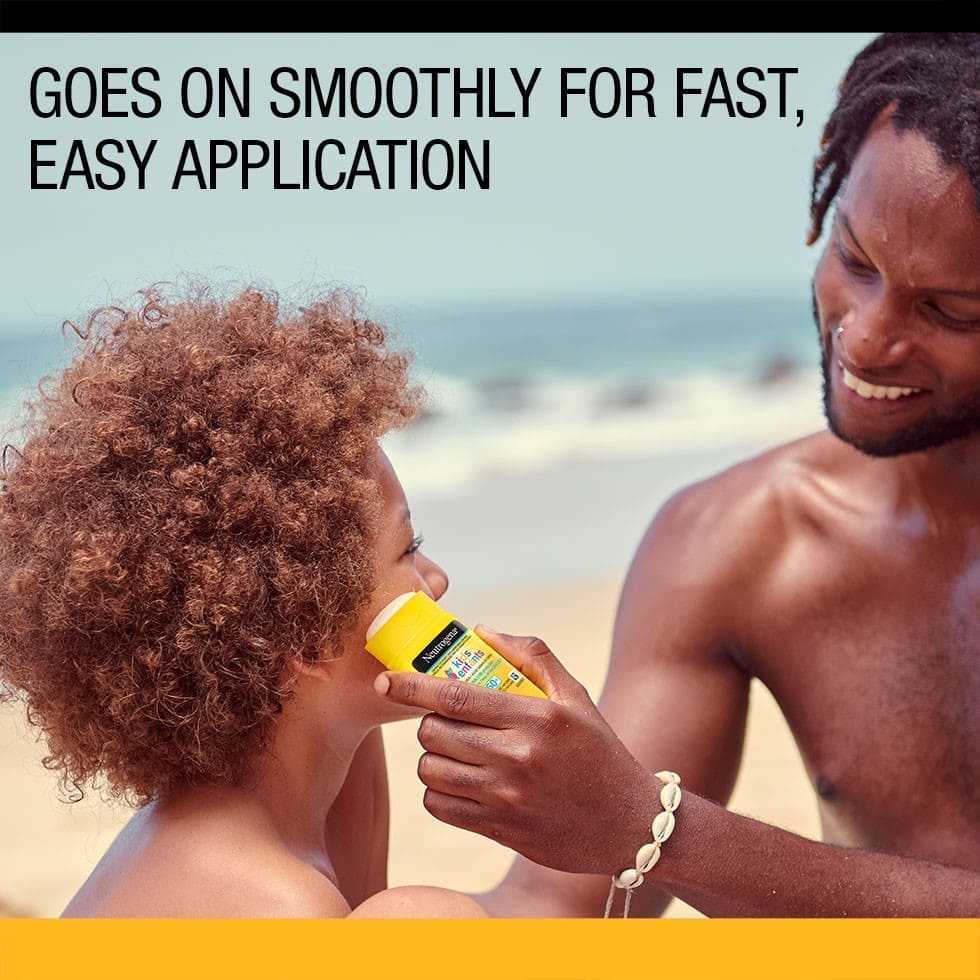 Father using sunscreen stick on his kid’s face on the beach