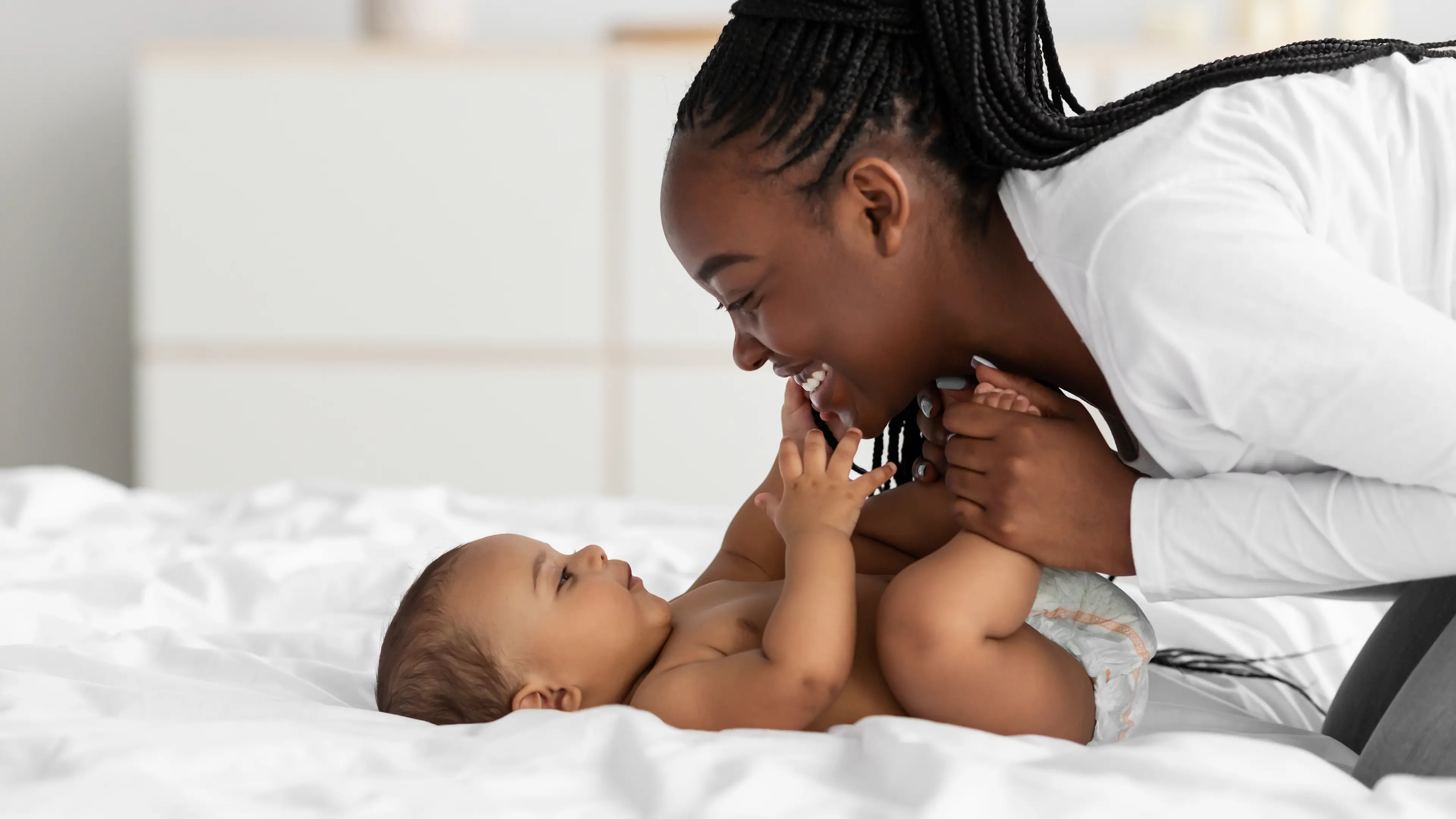 Jeune mère changeant la couche de son bébé au lit et souriant.