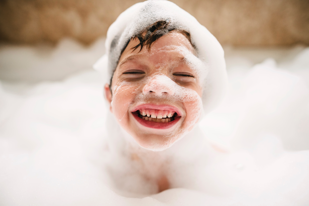 A happy young kid taking a bubble bath and smiling