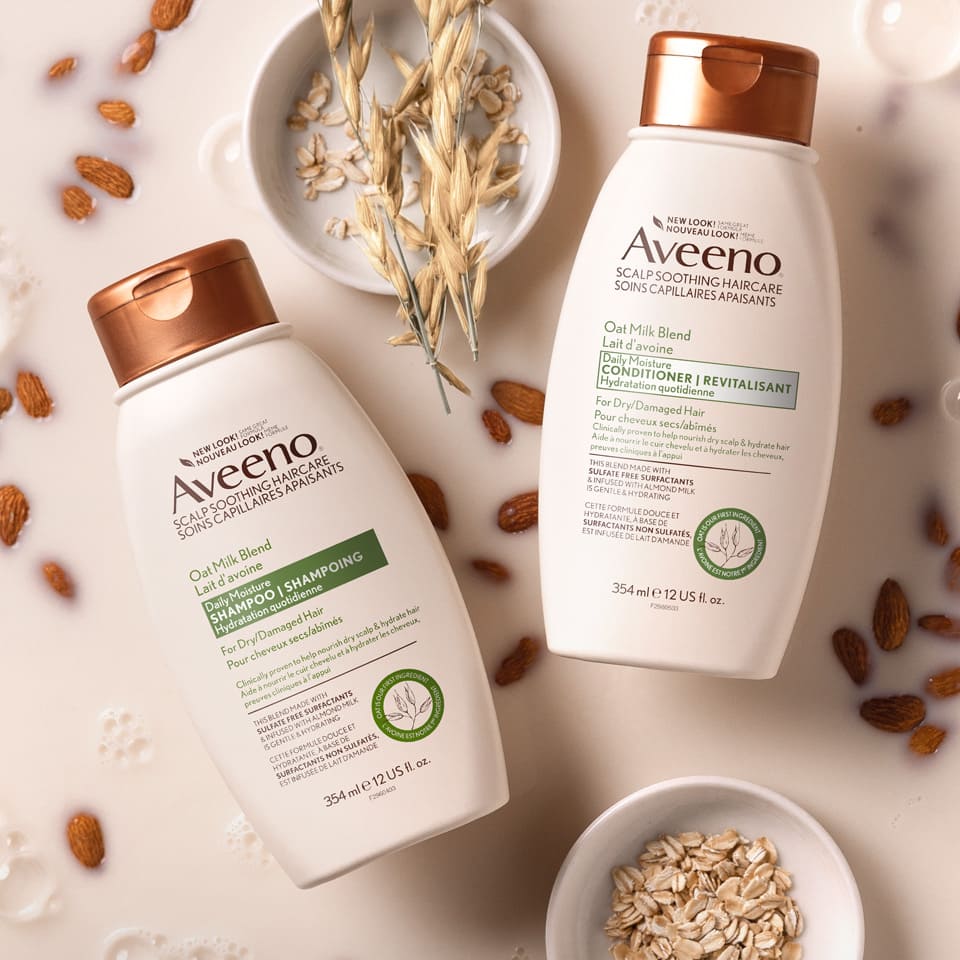 Flacons du shampoing et du revitalisant AVEENO® Lait d'avoine Hydratation quotidienne, avec de l’avoine et des amandes trempées dans du lait d’avoine en arrière-plan.