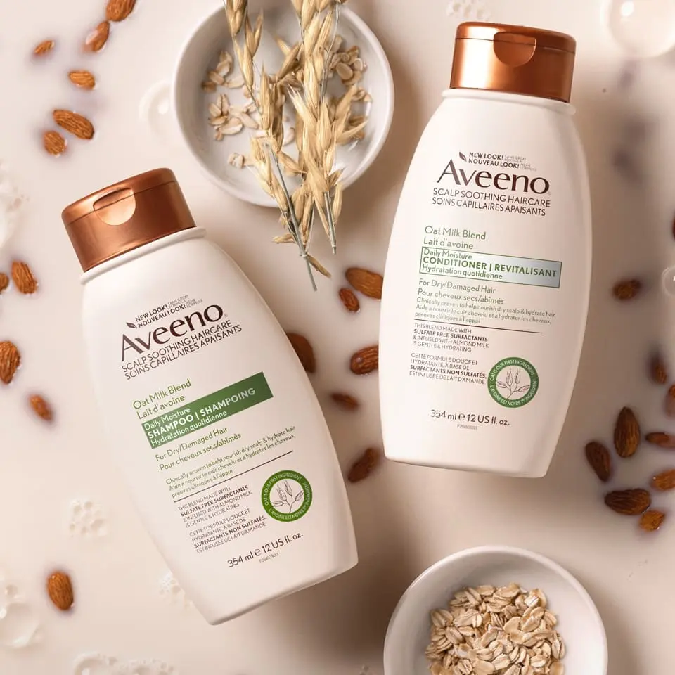 Flacons du shampoing et du revitalisant AVEENO® Lait d'avoine Hydratation quotidienne, avec de l’avoine et des amandes trempées dans du lait d’avoine en arrière-plan.