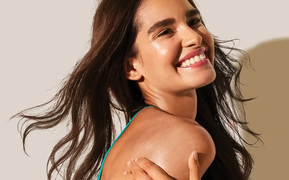 woman with long brown hair smiling against a beige backdrop