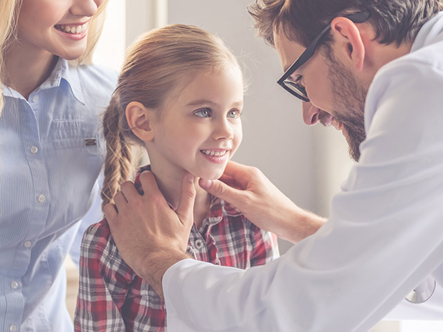 Une maman debout à côté d’un médecin examinant son enfant 