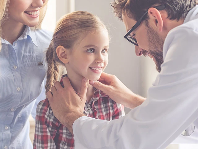 Une maman debout à côté d’un médecin examinant son enfant