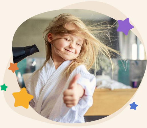 Child blowing her hair with a hairdryer and smiling.