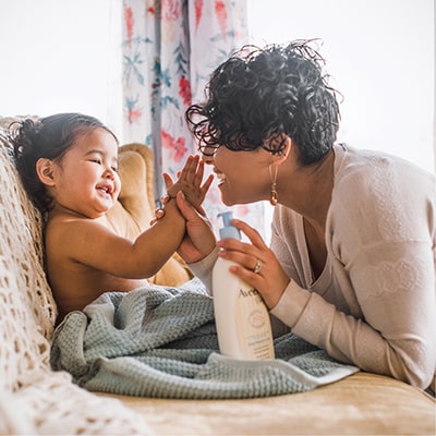 Une maman souriante qui utilise un produit AVEENO® BABY sur son bébé