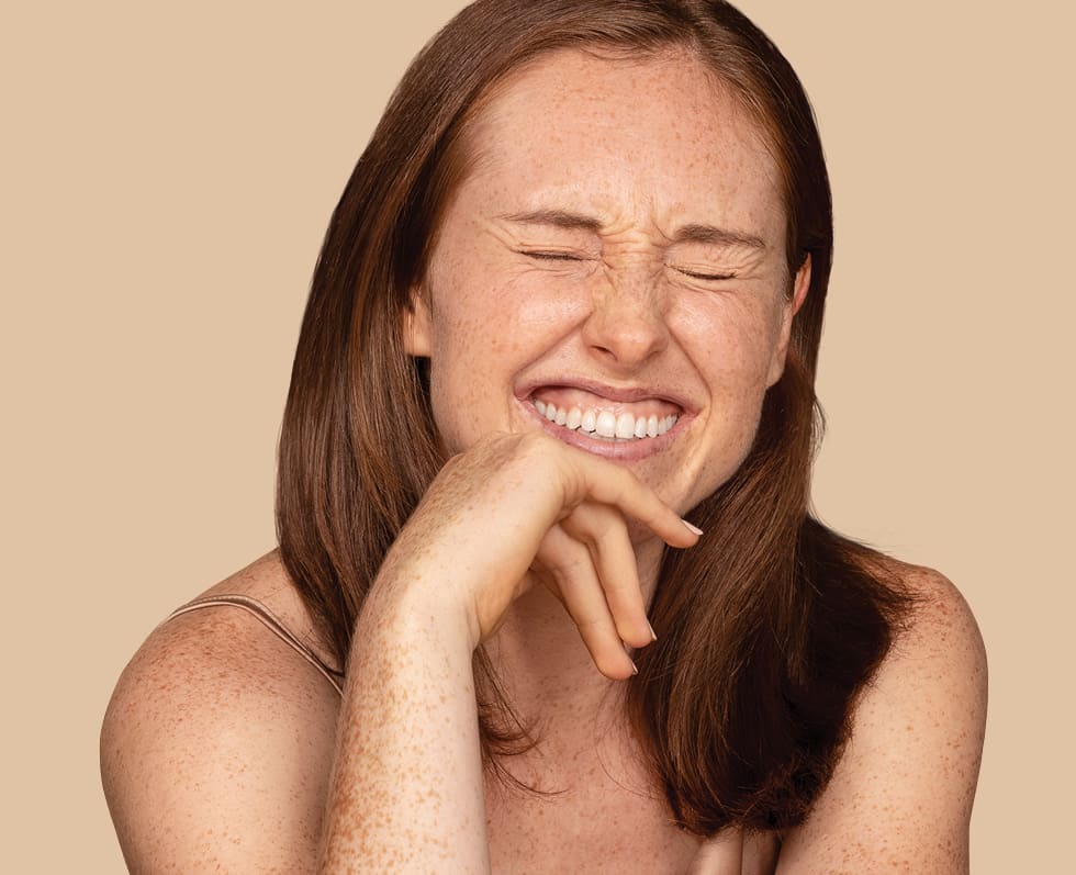 Femme aux longs cheveux châtain clair, la main sur le menton, souriant les yeux fermés.