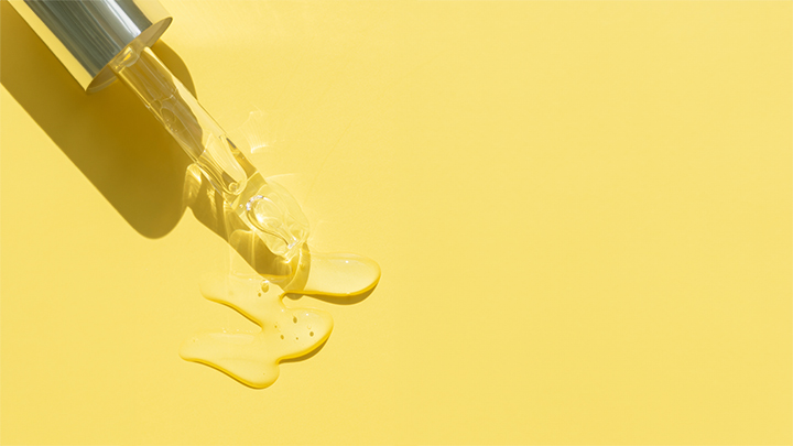 Banner including a close up of pipette with pouring liquid serum with a yellow background