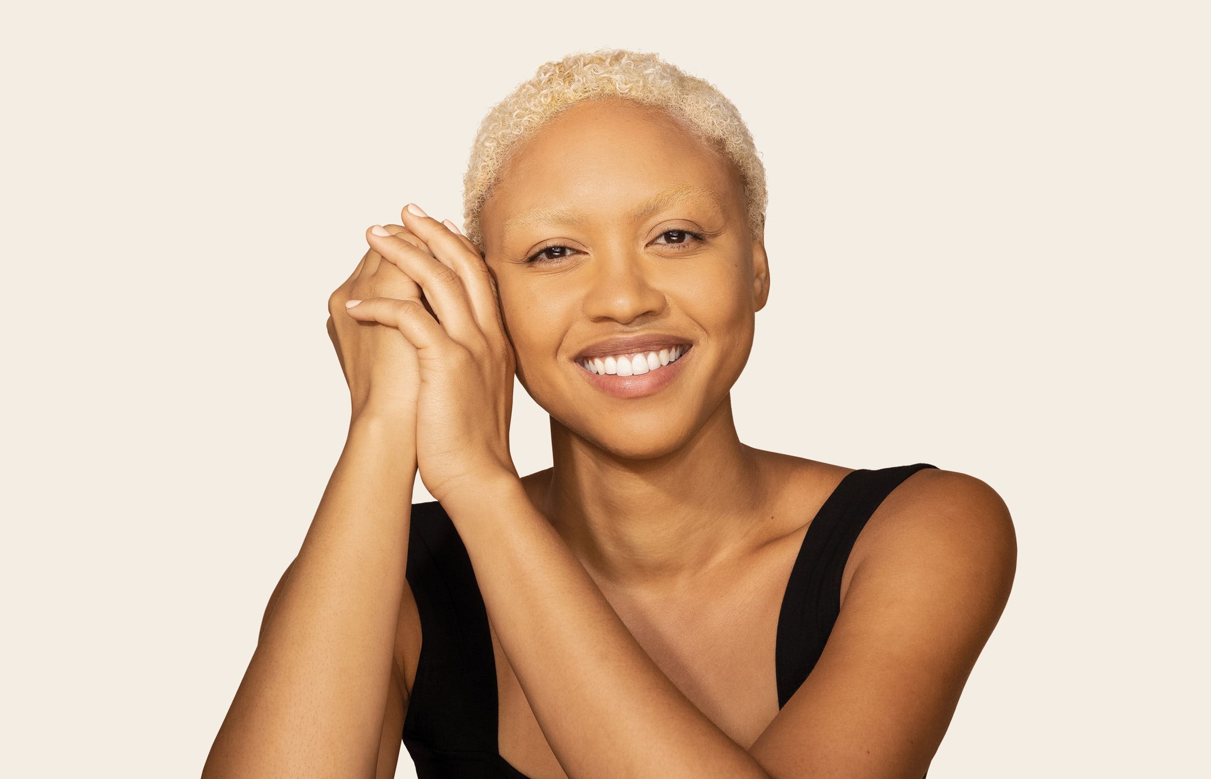 Woman with short blond hair holding her hands together over her cheek and smiling