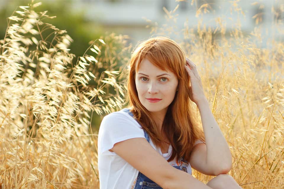 red hair woman in white shirt with hand againt her hair