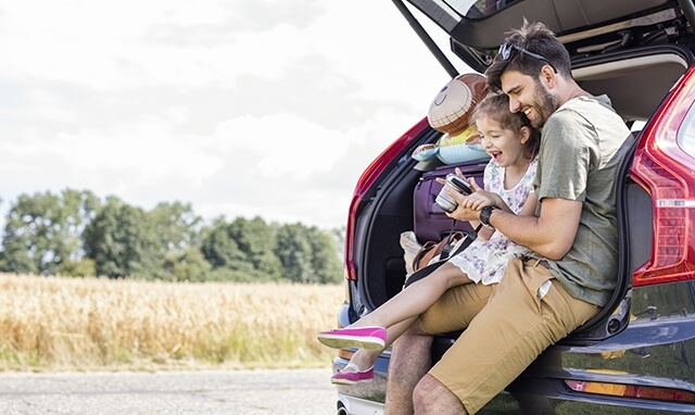 Dad with daughter by the family car on a trip