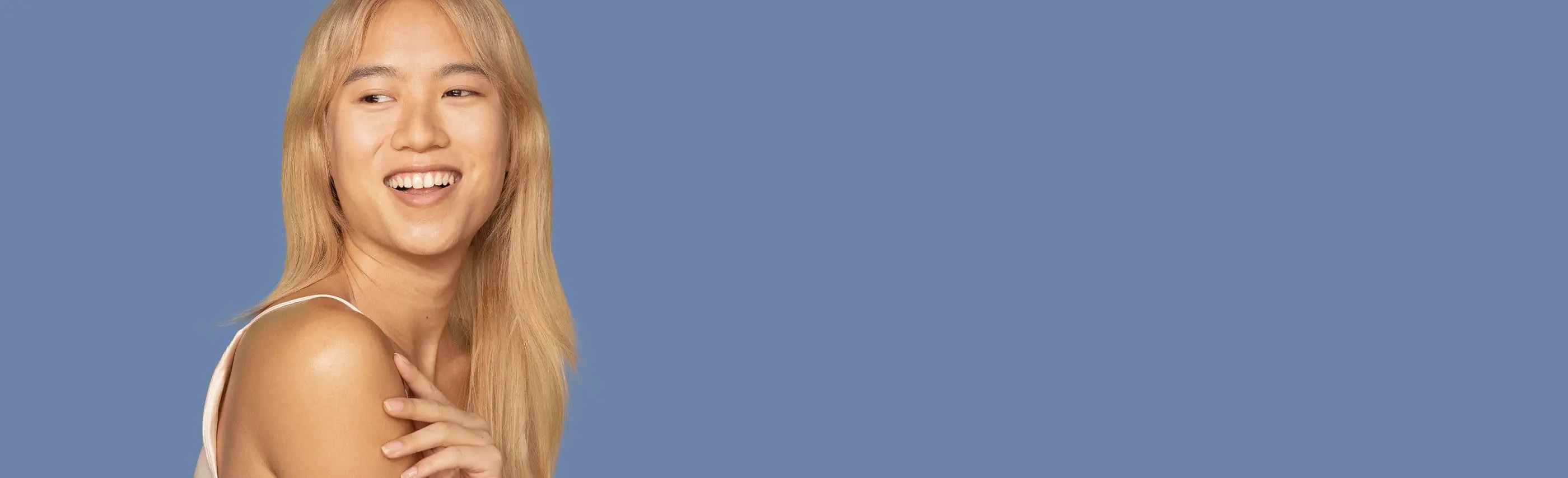 Woman with long blond hair looking over her shoulder and touching her right arm