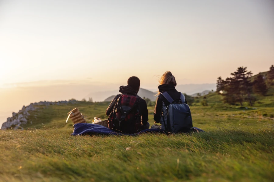 A man and woman sitting on a hill watching the sunset