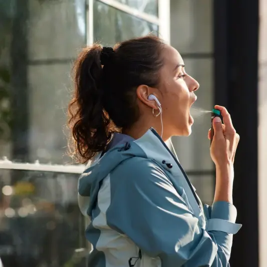 Une Femme utilisant la Vaporisateur buccal à la nicotine NICORETTE VapoÉclair SmartTrackMC dans sa bouche 
