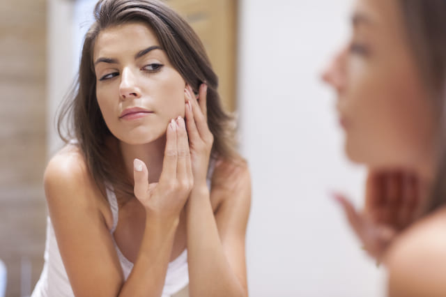 Femme qui regarde sa peau dans le miroir