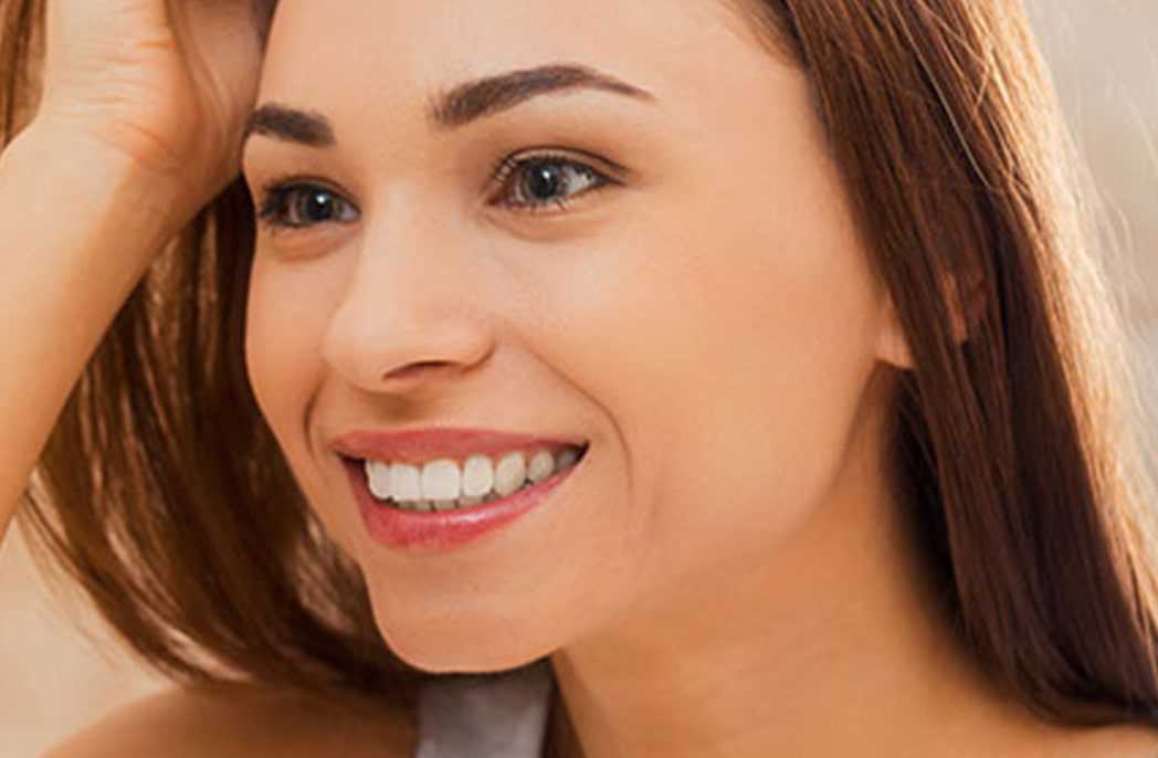 Une jeune femme souriante aux cheveux longs qui repose sa main sur sa tête