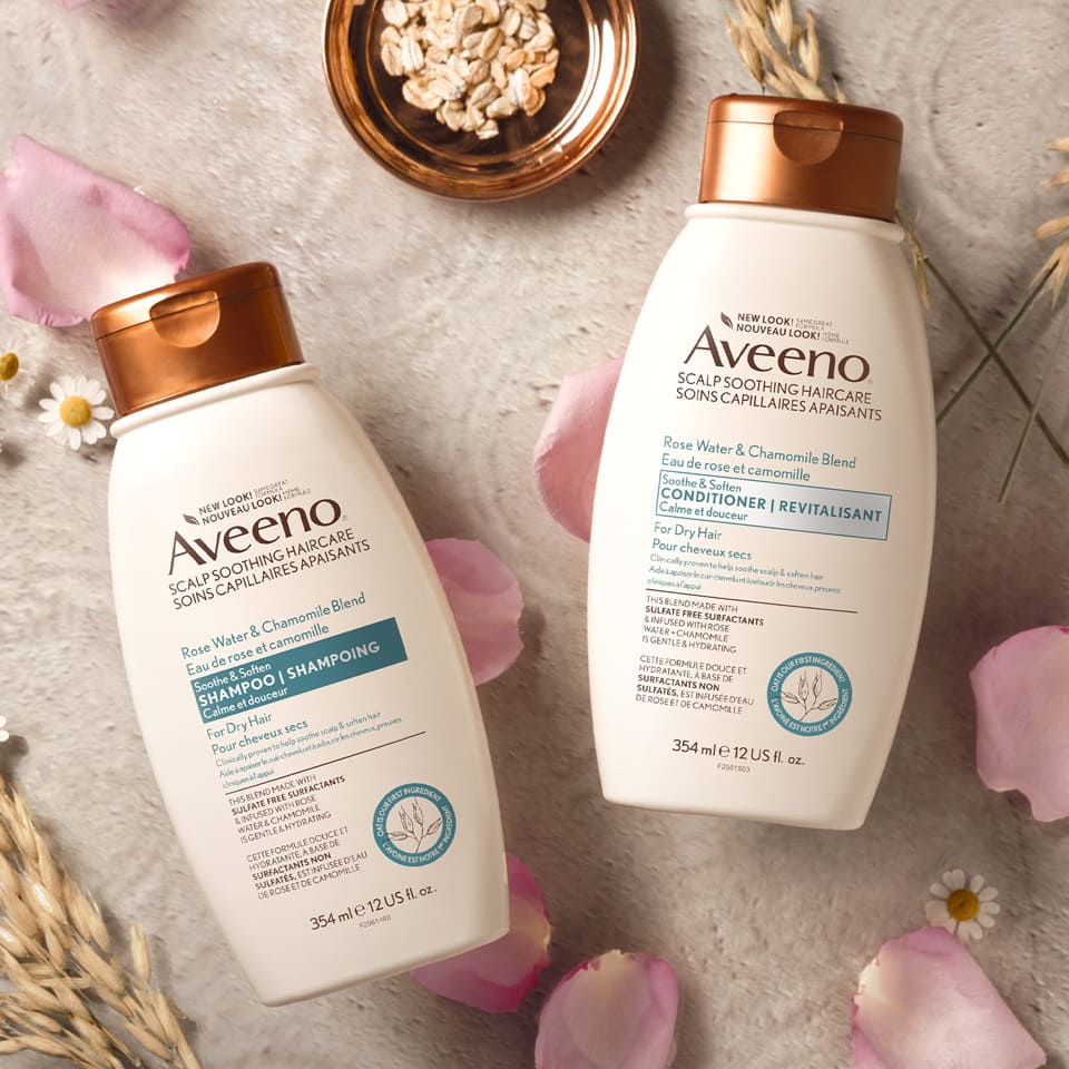 Flacons du shampoing et du revitalisant AVEENO® Eau de rose et camomille Calme et douceur, avec de l’avoine et des pétales de rose en arrière-plan.