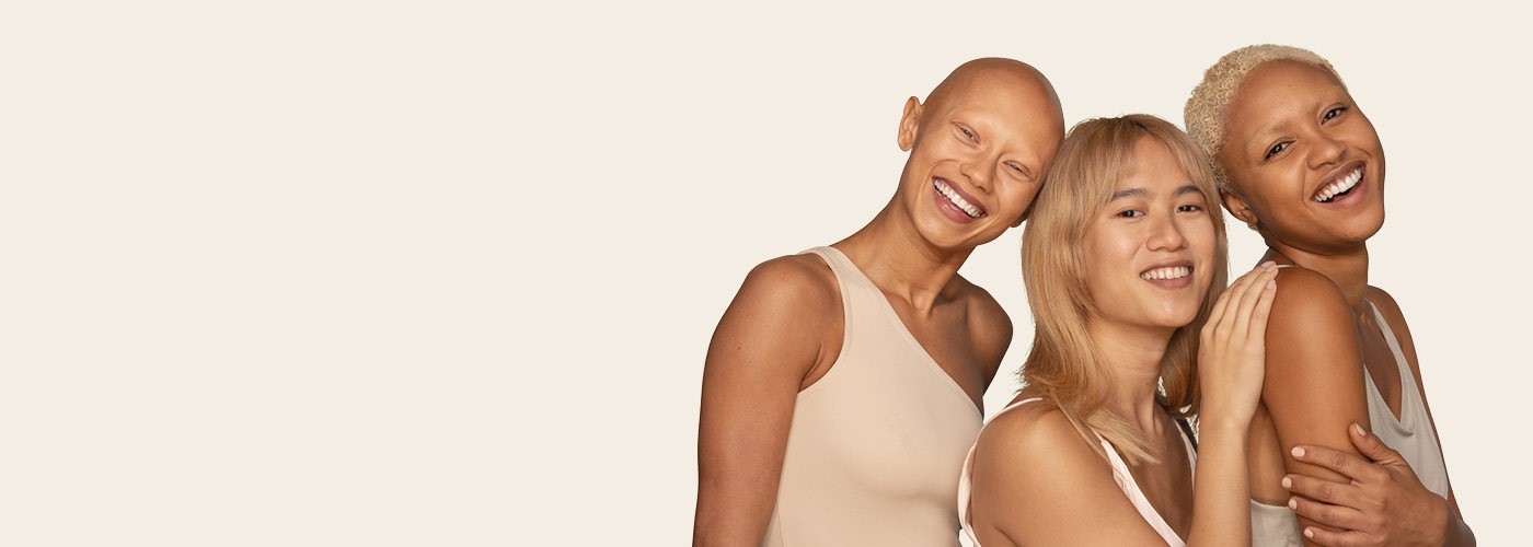 Three women from different ethnicities are standing together and smiling