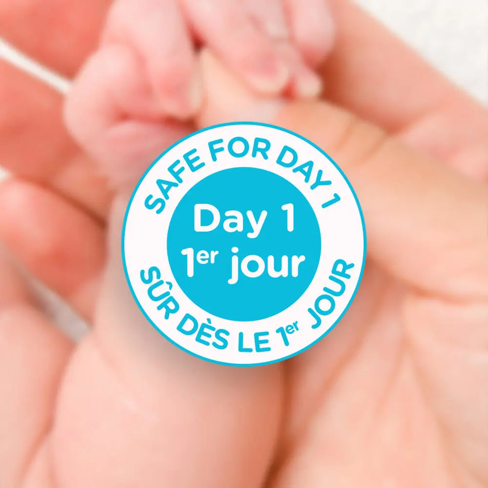 Allégation sur le produit Aveeno® Bébés indiquant « Sans danger dès le premier jour » et gros plan de la main d’un parent tenant la main de son nouveau-né en arrière-plan
