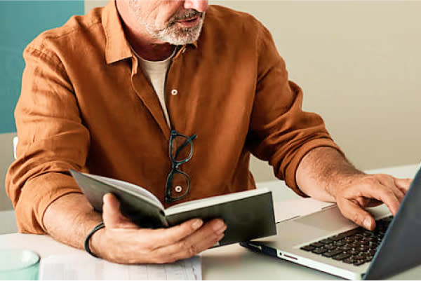 man typing at a computer and looking at a book