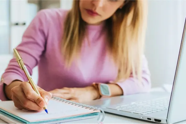 Women sitting at a computer writing on a pad of paper