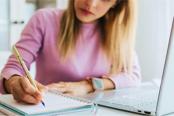 Women sitting at a computer writing on a pad of paper