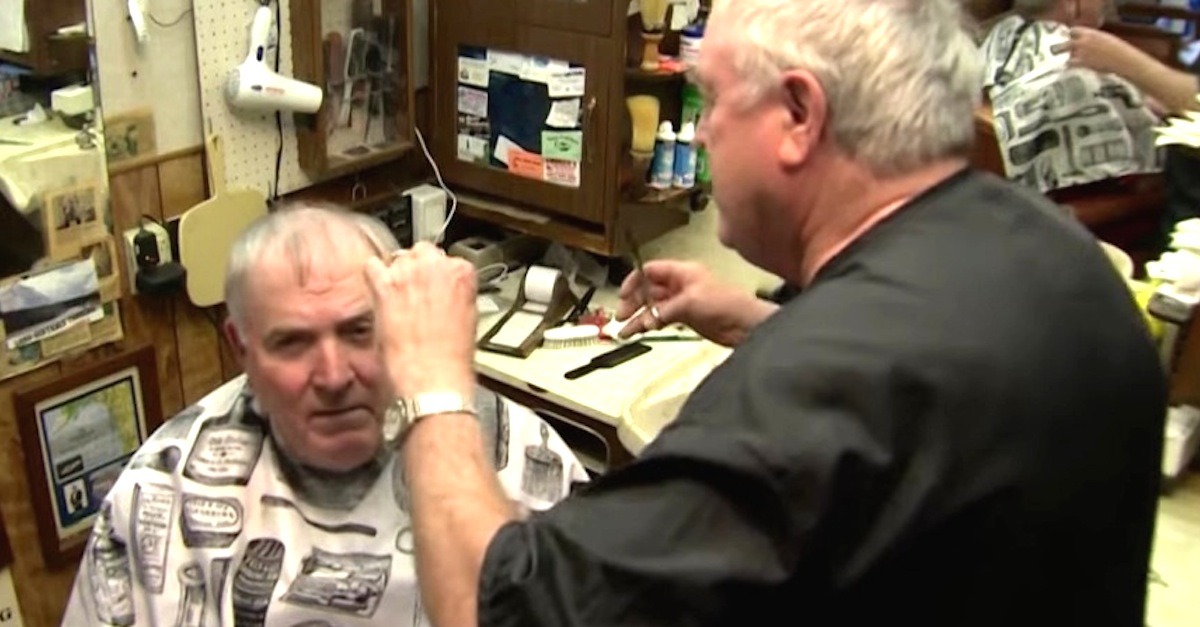 He Sits Down In The Barber Chair. But Look Closely At The Man Cutting His Hair...