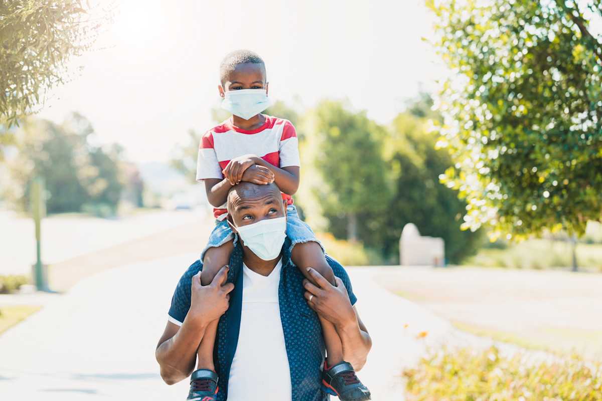 Dad gives son piggy back ride; both wear masks Dad gives son piggy back ride; both wear masks
