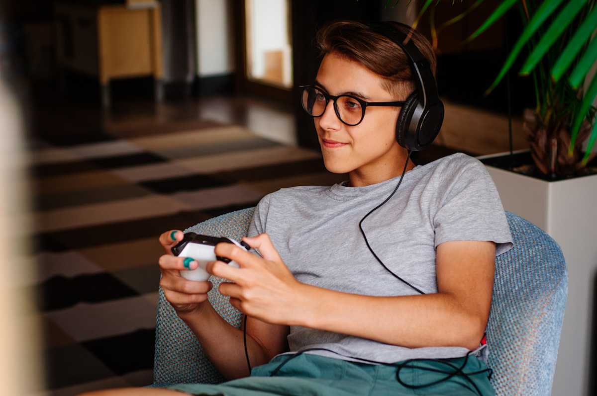 Smiling teenager boy in glasses and headphones playing game console Smiling teenager boy in glasses and headphones playing game console