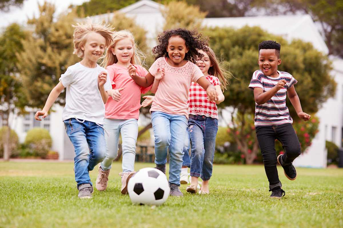 Group Of Children Playing Football With Friends In Park Group Of Children Playing Football With Friends In Park