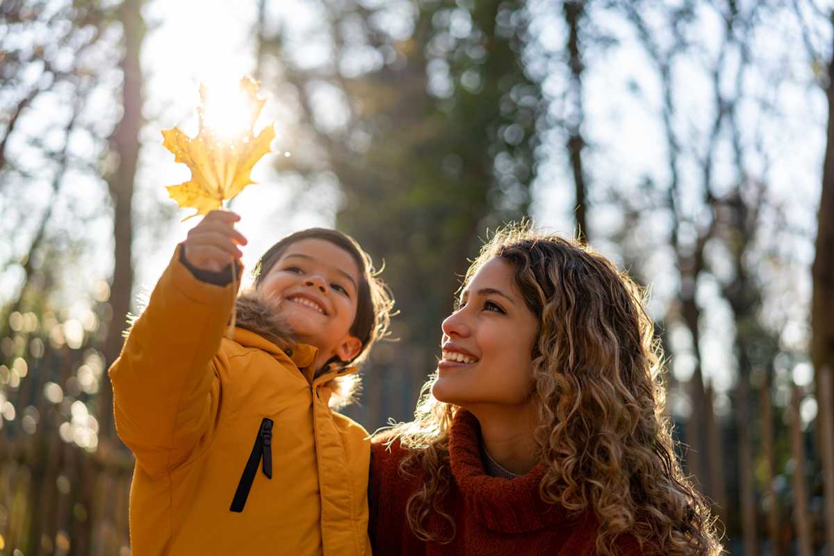 Beautiful mother looking at a leaf her son is holding on a sunny autumn day at the park Beautiful mother looking at a leaf her son is holding on a sunny autumn day at the park