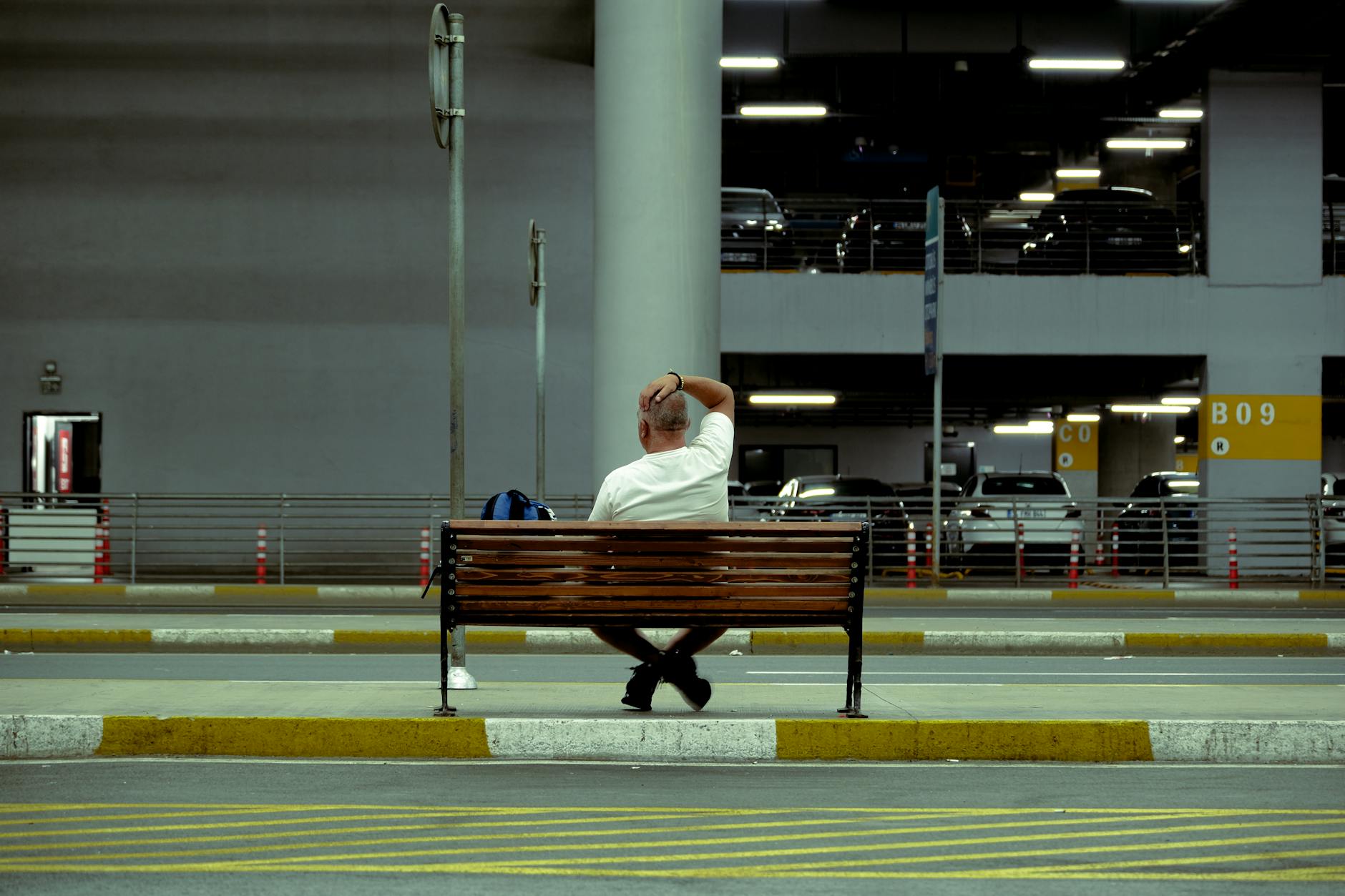 A man sitting alone on a bench in a parking area, urban solitude.