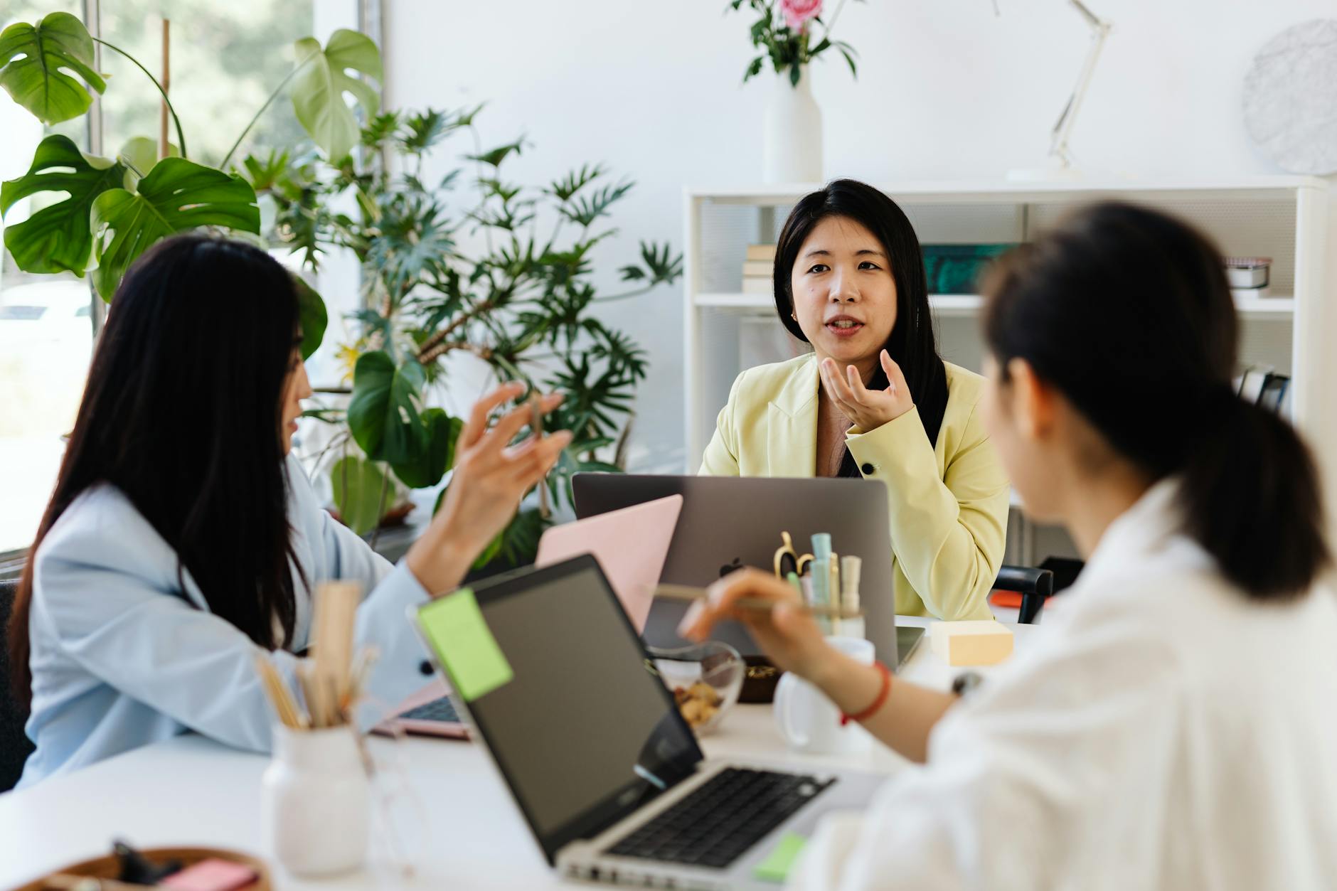 Three businesswomen engaged in discussion over laptops in a modern office setting.