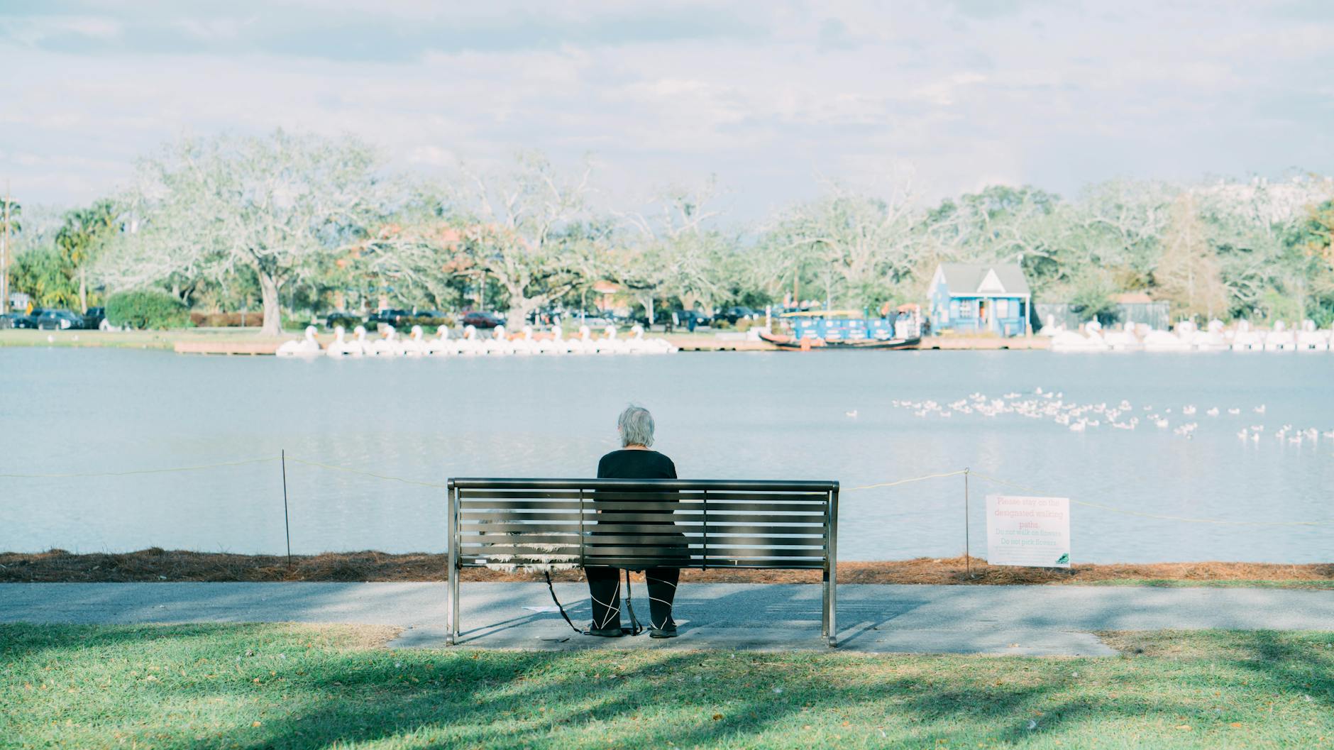 Serene scene of a senior woman sitting alone on a bench by a lake in New Orleans park.