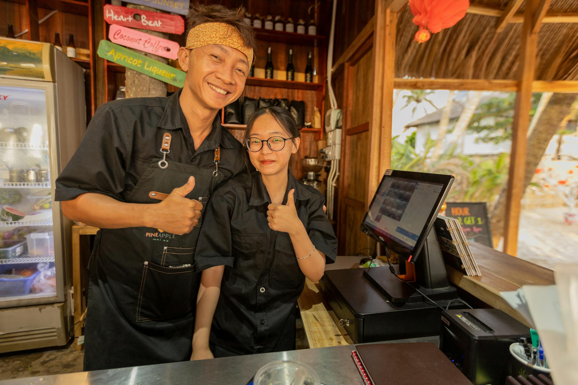Smiling staff at a tropical beach bar giving thumbs up, creating a welcoming atmosphere.