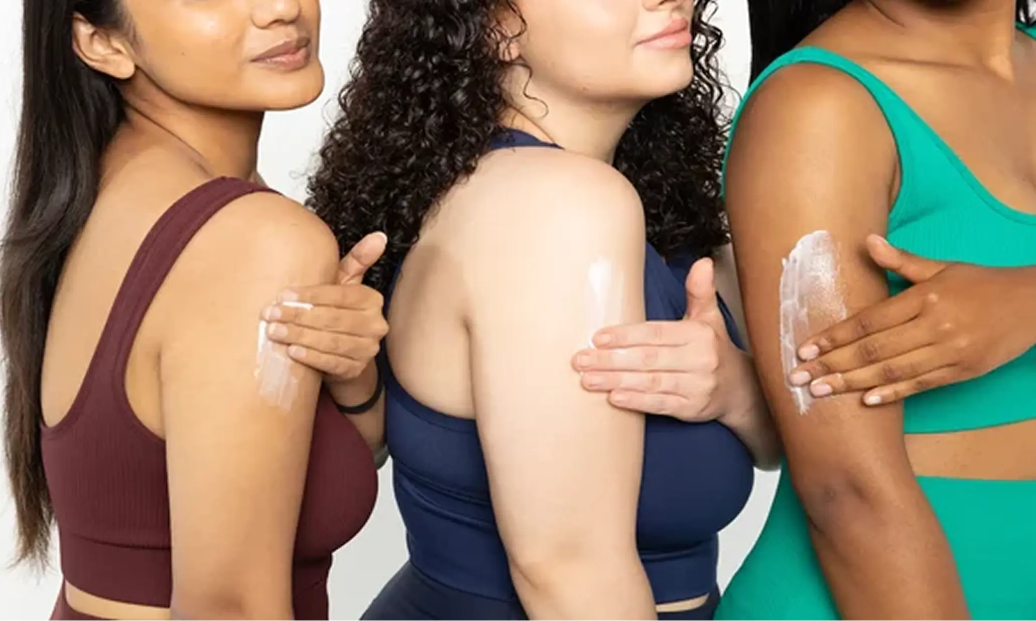A group of woman applying cream on her arms and posing for a photo