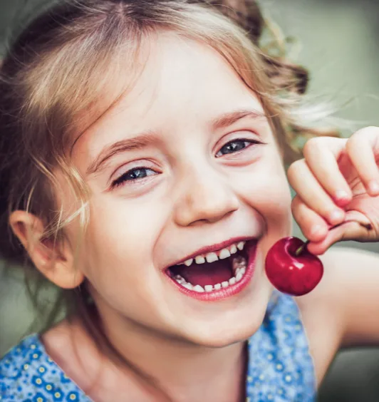 Mädchen mit schönen geraden Zähnen isst eine Kirsche