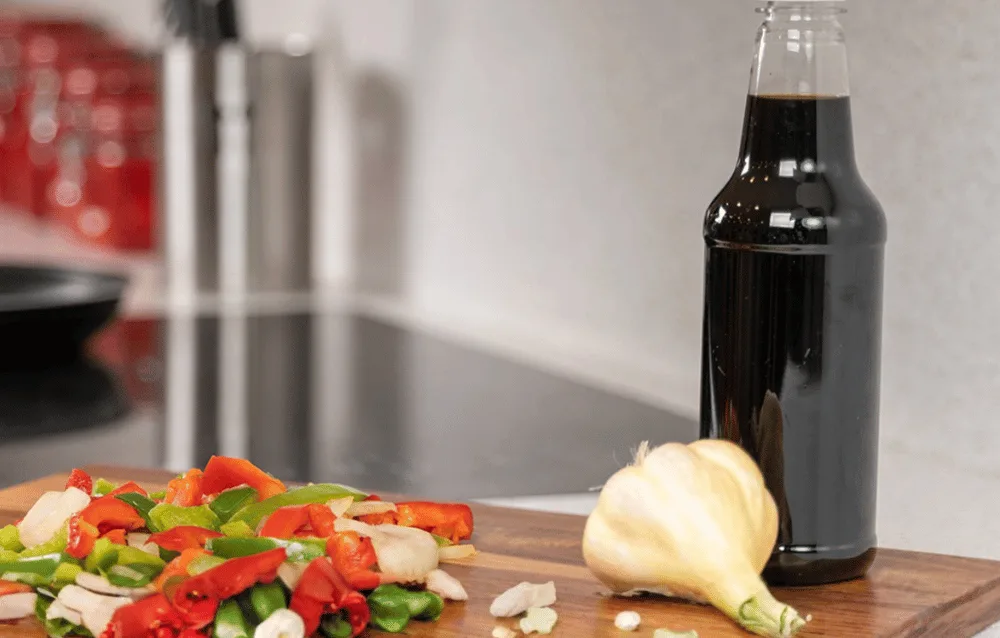 Chopped vegetables and dark sauce bottle on cutting board