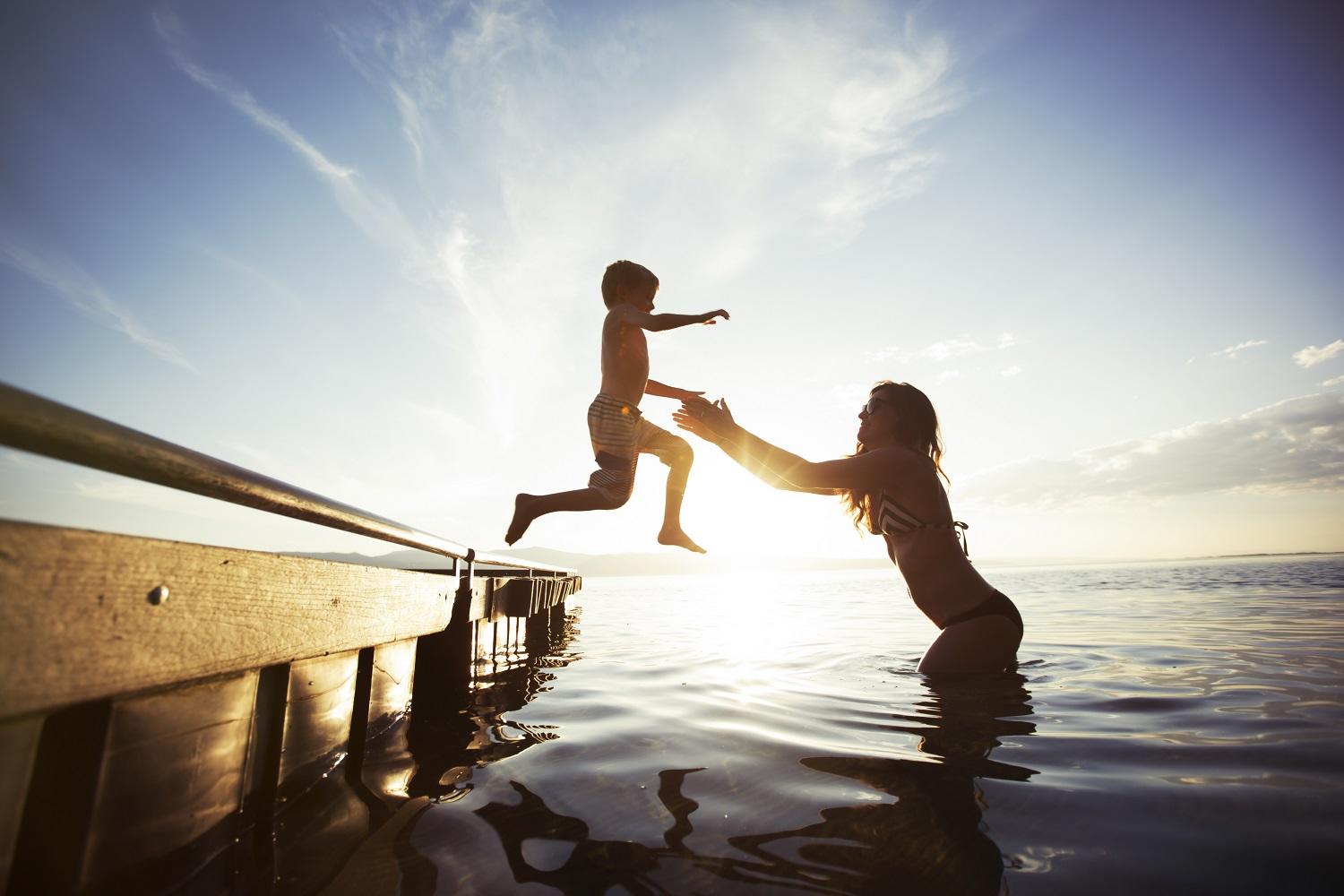 a young boy jumping from a jetty into his mother's arms