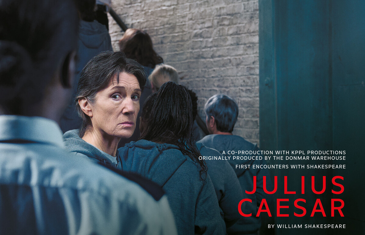 Harriet Walter, dressed in a prison uniform, looks over her shoulder at the camera. In the foreground is a prison officer.