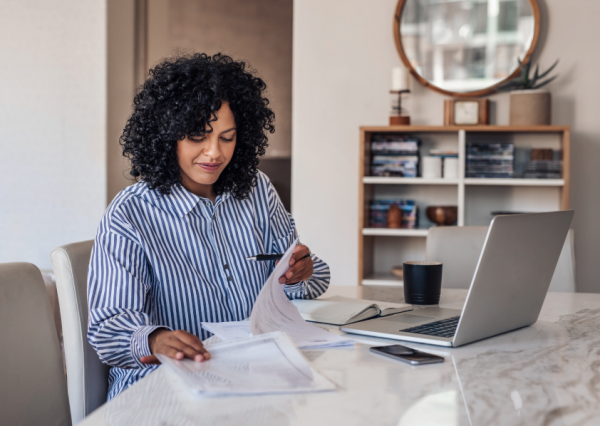 Woman sitting at a table with laptop, looking down at paperwork