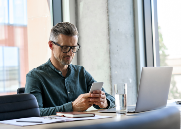 Smiling mature businessman holding smartphone sitting in office