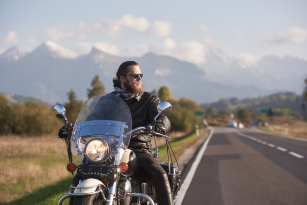 A young man on a motorcycle, looking into the distance with mountain scenery behind him 